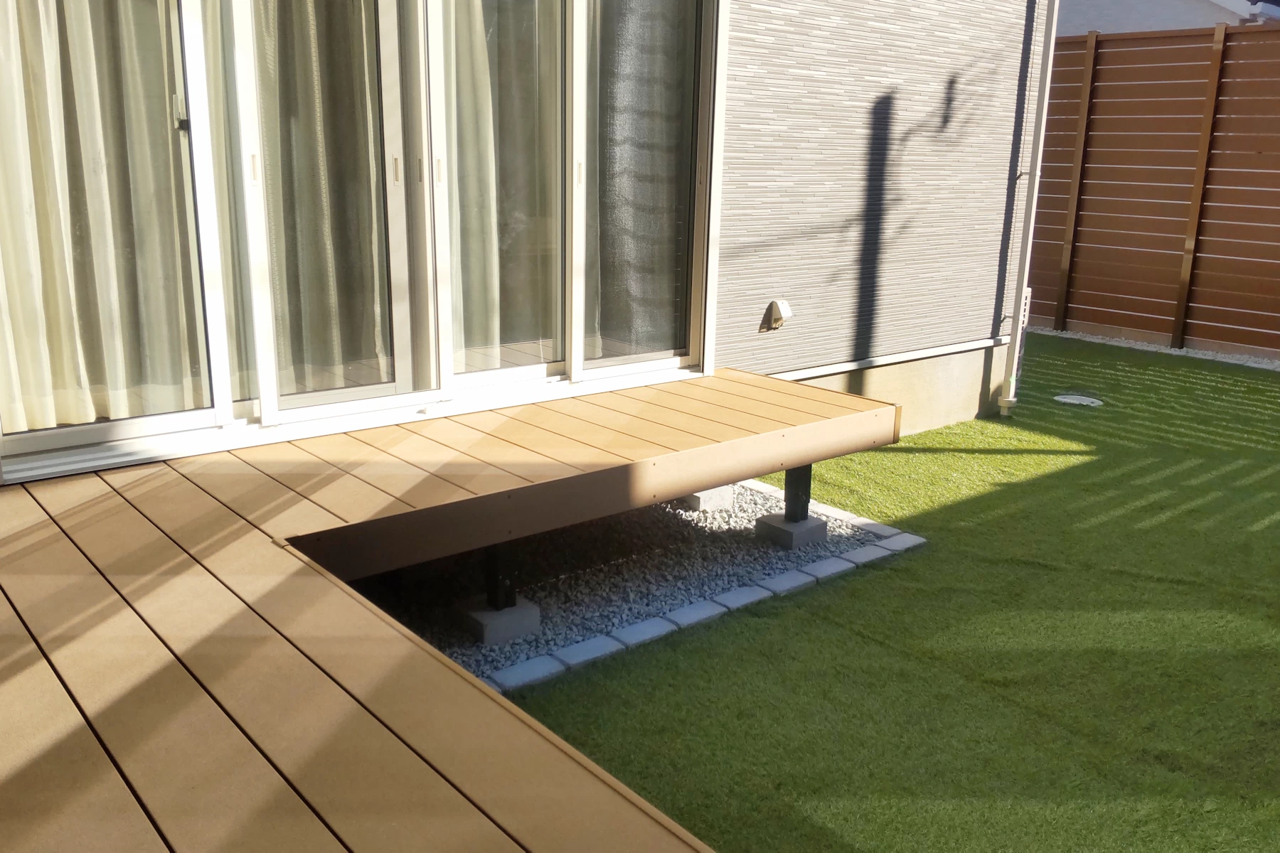 LIXILの人工木デッキ「樹ら楽ステージ」をL字型に配置し、室内と庭をつなぐ開放的なアウトドアリビング。